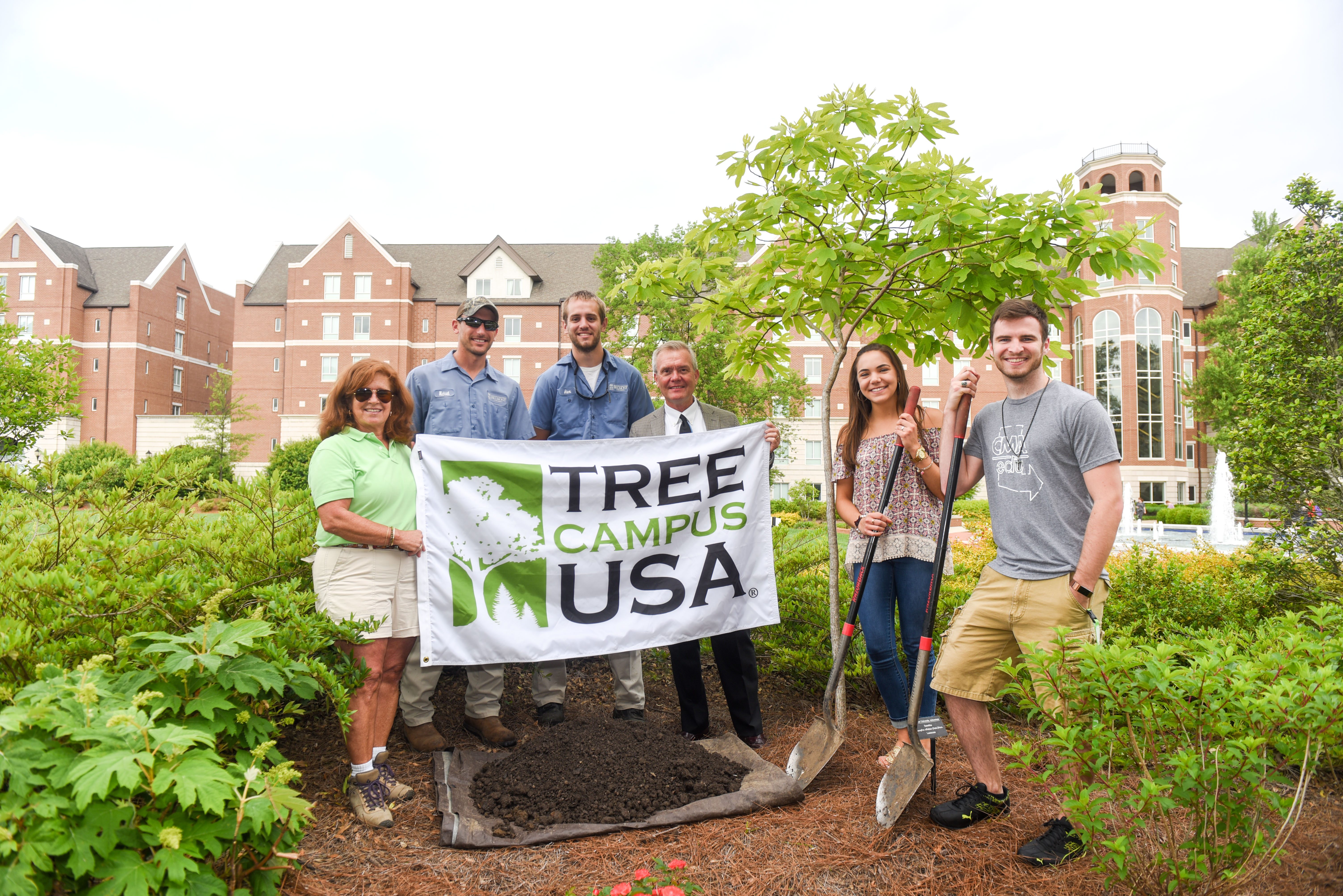 Students and staff pose for a picture in front of a sassafras tree and the USA Tree Campus sign.