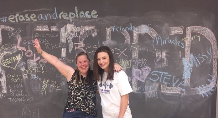 A Belmont student (right) poses with her community buddy (left) in front of a chalkboard that has been decorated.