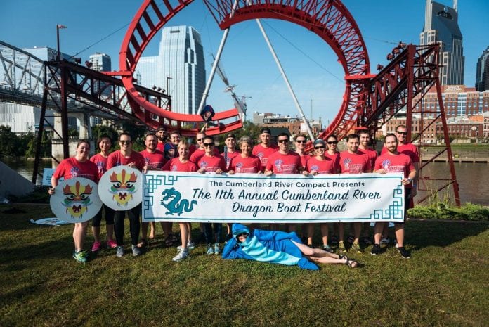 Massey 2017 Dragon Boat race team posing in front of a rollercoaster, holding a banner for the event.