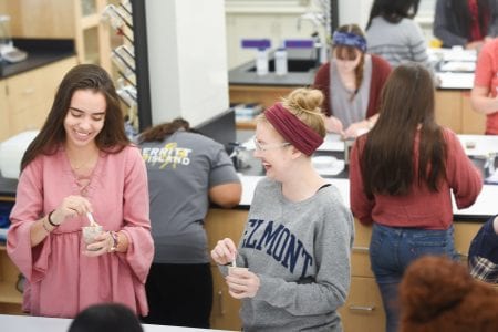 two female students laughing while mixing ingredients in a cup