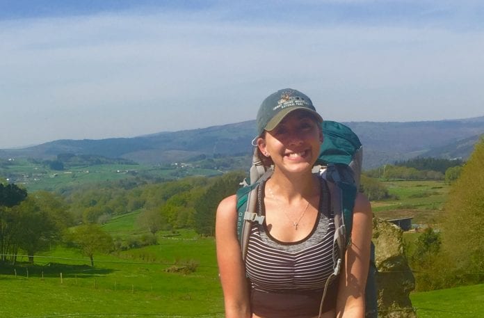 Erin Sanislo, carrying hiking backpack, with rolling hills behind her