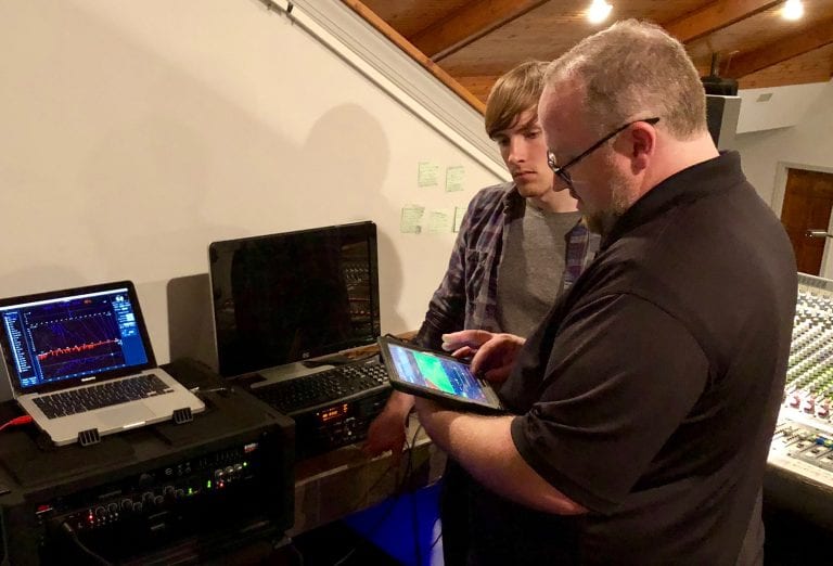 two men looking at tablet, with computers in the background