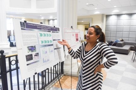 student points to her poster, smiling