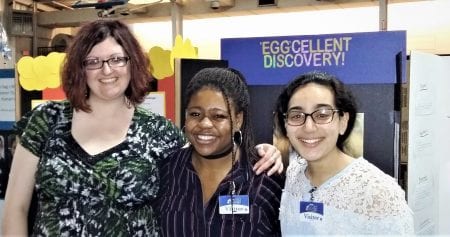 Both students and Dr. Garrett pose for a picture in front of a science fair poster.