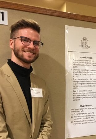 Student Eason Taylor poses in front of a poster at a research presentation.