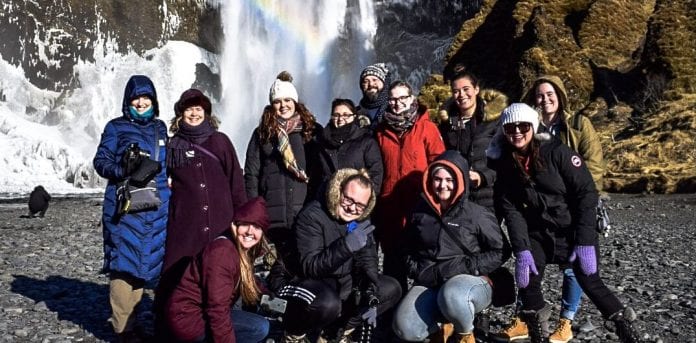 students and faculty, bundled in winter clothes, posing in front of a waterfall