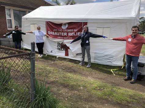 Volunteers stand at a distance in front of food distribution tent