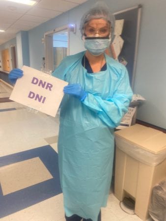 Stahl in scrubs holding a sign that reads "DNR DNI"