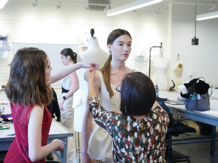Fashion student and professor adjust clothing on a model at a Fashion Show fitting.