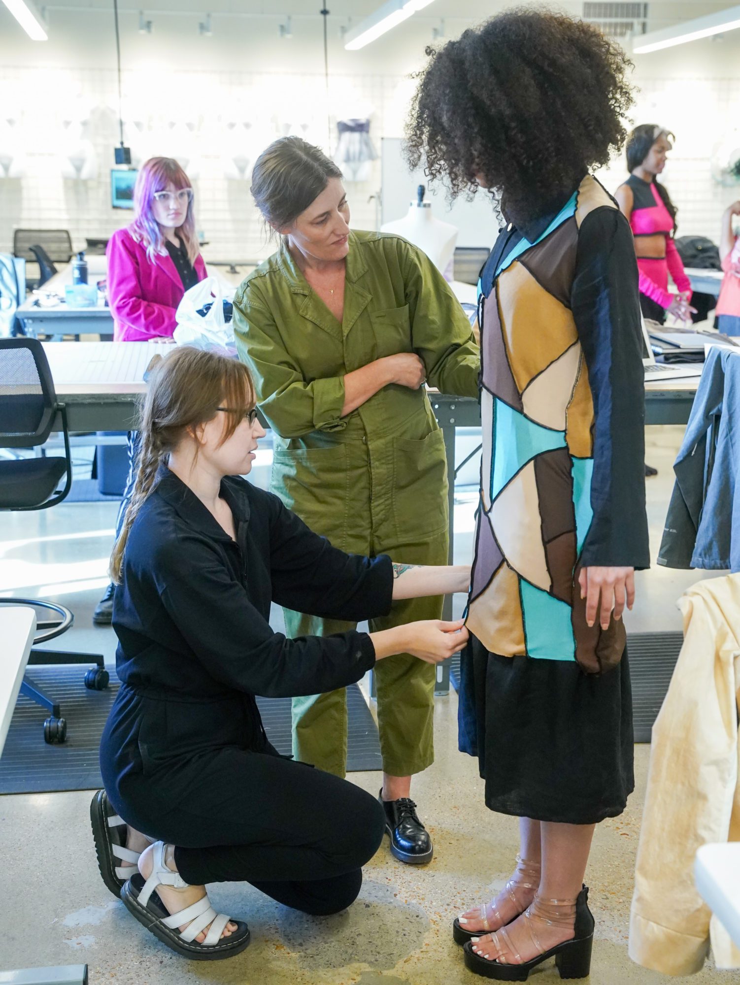 Fashion student Kat Westmoreland kneels in front of a model wearing her design to adjust a hem. 