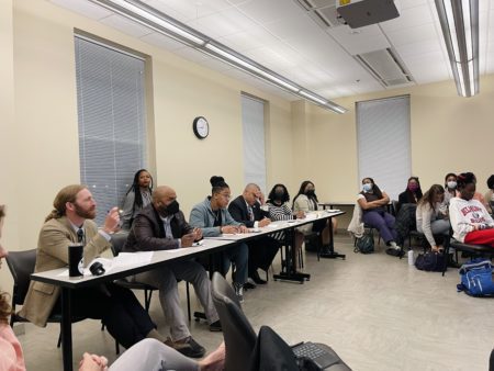 A group of panelists at a long table including professors from Belmont, Vanderbilt and Fisk listen to student presentations during the Bridging the Gap course.