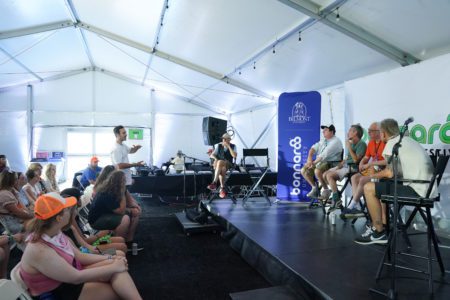 Students sit in chairs facing a small stage in the media room at Bonnaroo where a panel discussion is happening.