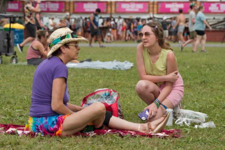 Belmont student Hailey Pierce kneels beside a woman sitting on the grass at Bonnaroo. 