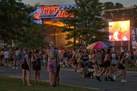 A neon sign lights up the That Tent at Bonnaroo as attendees watch the band on stage. 