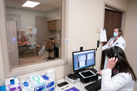 woman looking through simulation lab window at actor patient